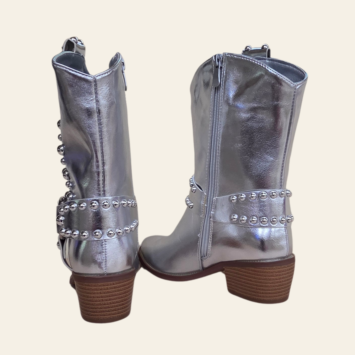 A pair of metallic silver western-style boots with brown stacked block heels and silver rhinestone embellishments, shown from the back against a light beige background.