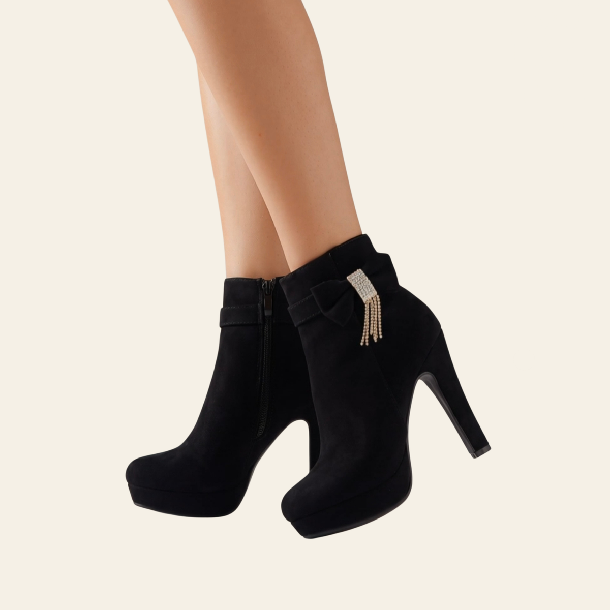 A pair of black suede high-heeled ankle boots with platform soles, shown on a model's feet against a light cream background. One boot features a decorative silver rhinestone-embellished strap with dangling rhinestone tassels.