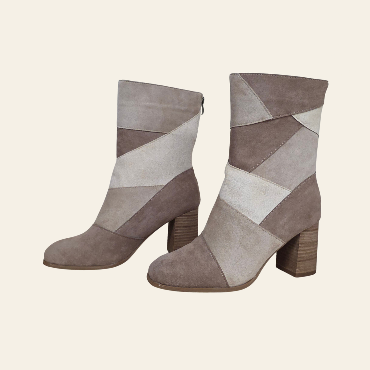 A pair of mid-calf ankle boots with a geometric patchwork design in taupe, beige, and off-white suede-like panels, featuring a chunky block heel, shown against a solid cream background.