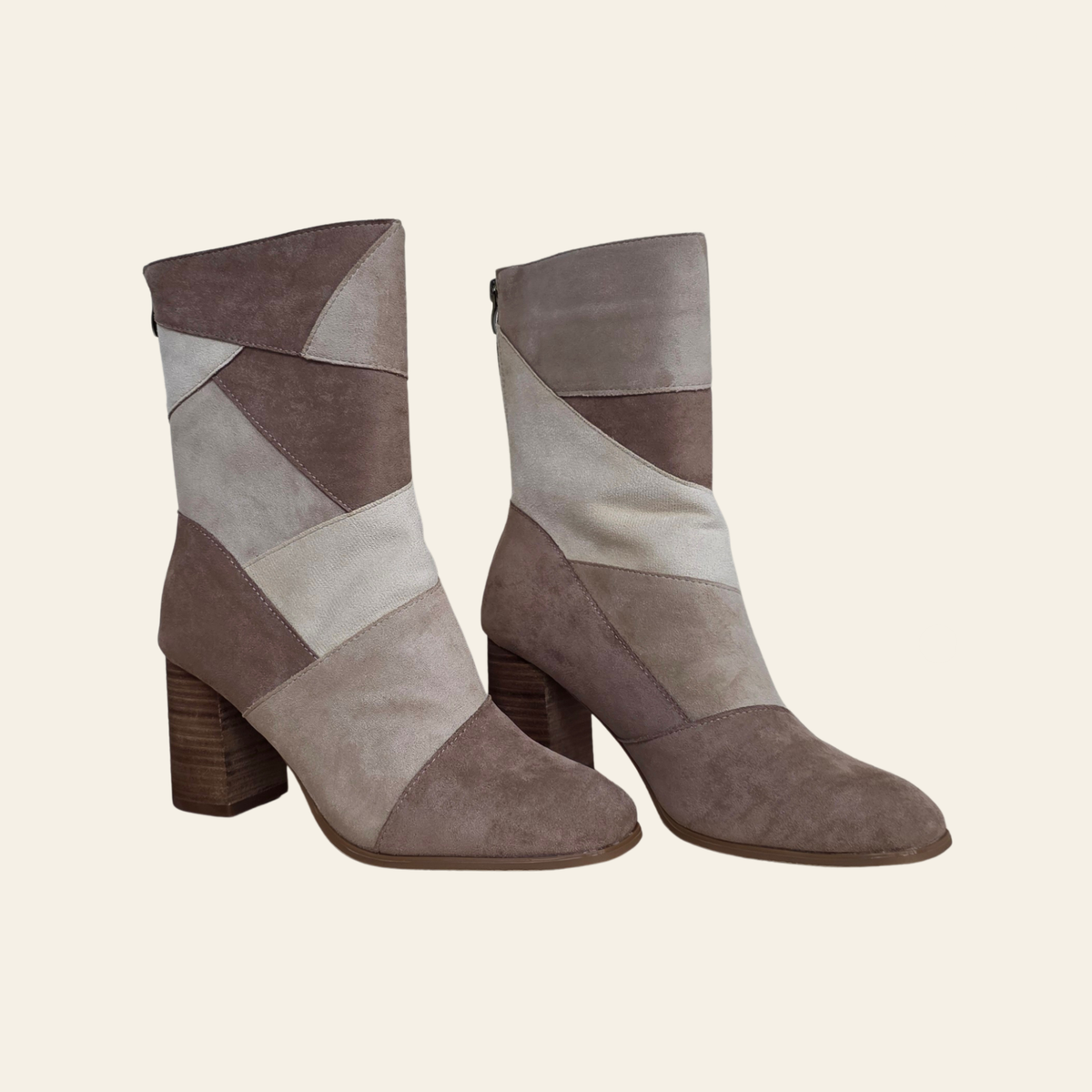 A pair of mid-calf ankle boots with a geometric patchwork design in taupe, brown, and cream suede, featuring a chunky block heel, shown against a solid light beige background.