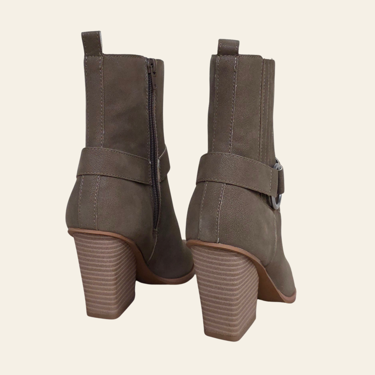 A pair of taupe-brown suede ankle boots with side zippers and buckle straps, shown from the back against a light cream background.