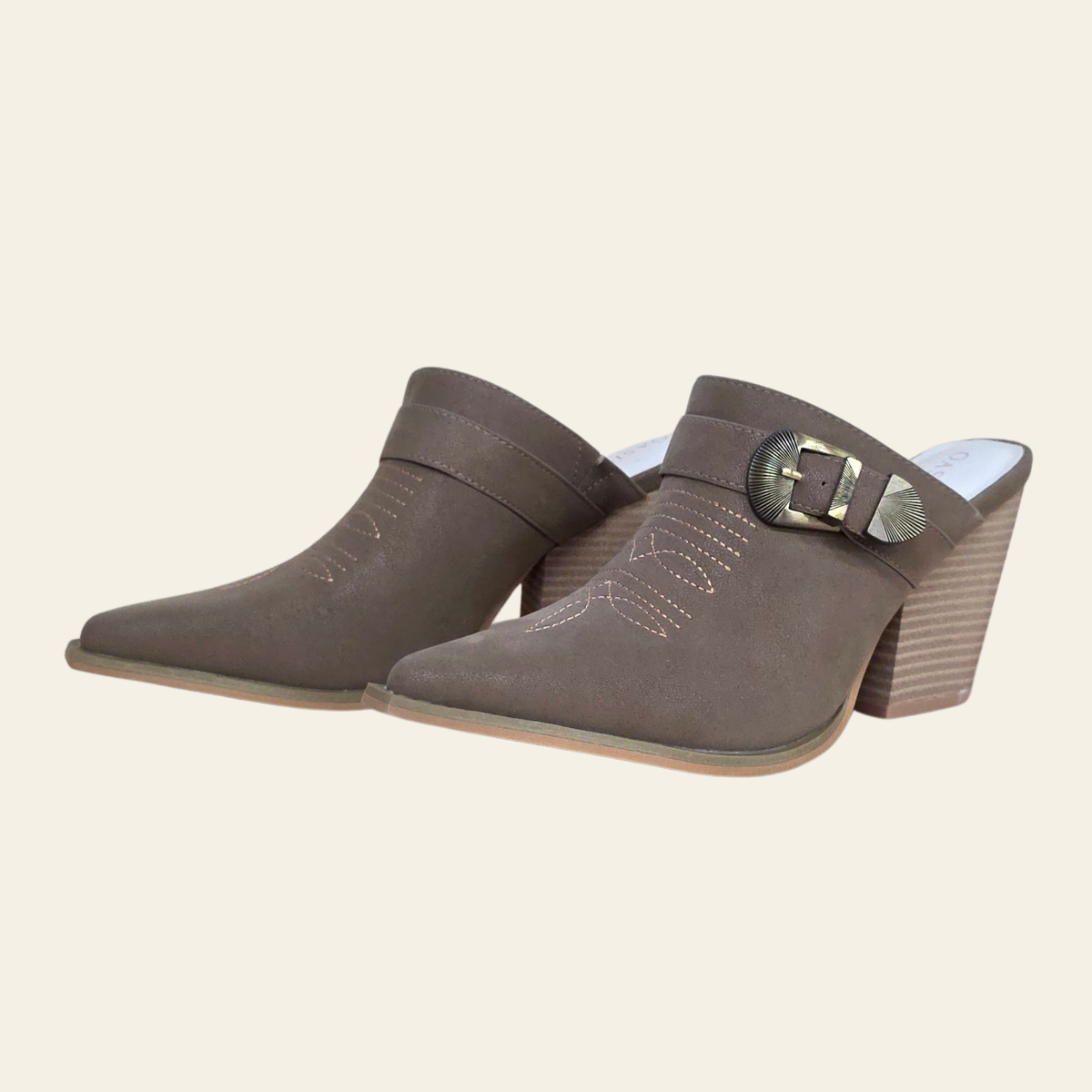 A pair of women's pointed-toe mule heels in taupe-brown faux suede, featuring decorative stitching, a matching ankle strap with a silver-tone buckle, and stacked block heels, shown against a solid cream background.