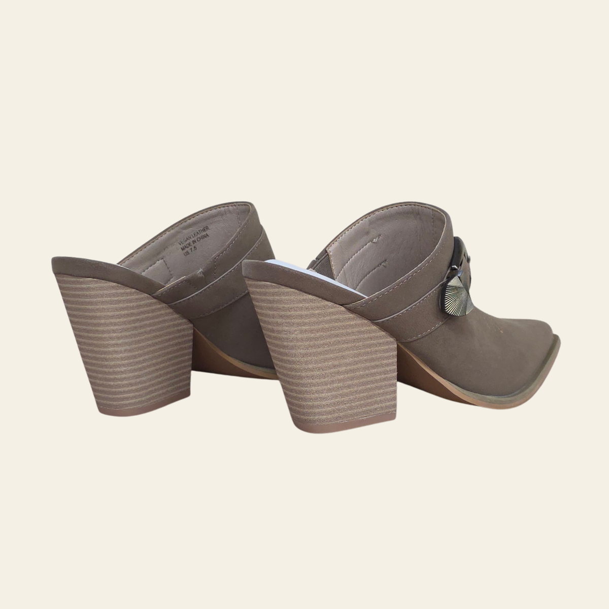 A pair of taupe-brown block-heeled mule sandals with a textured, ribbed wedge heel and a small metallic decorative accent on the strap, shown from a rear three-quarter angle against a solid cream background.