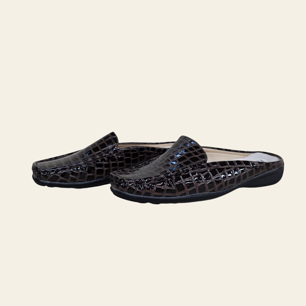 A pair of dark brown crocodile-embossed mule loafers on a light beige background.