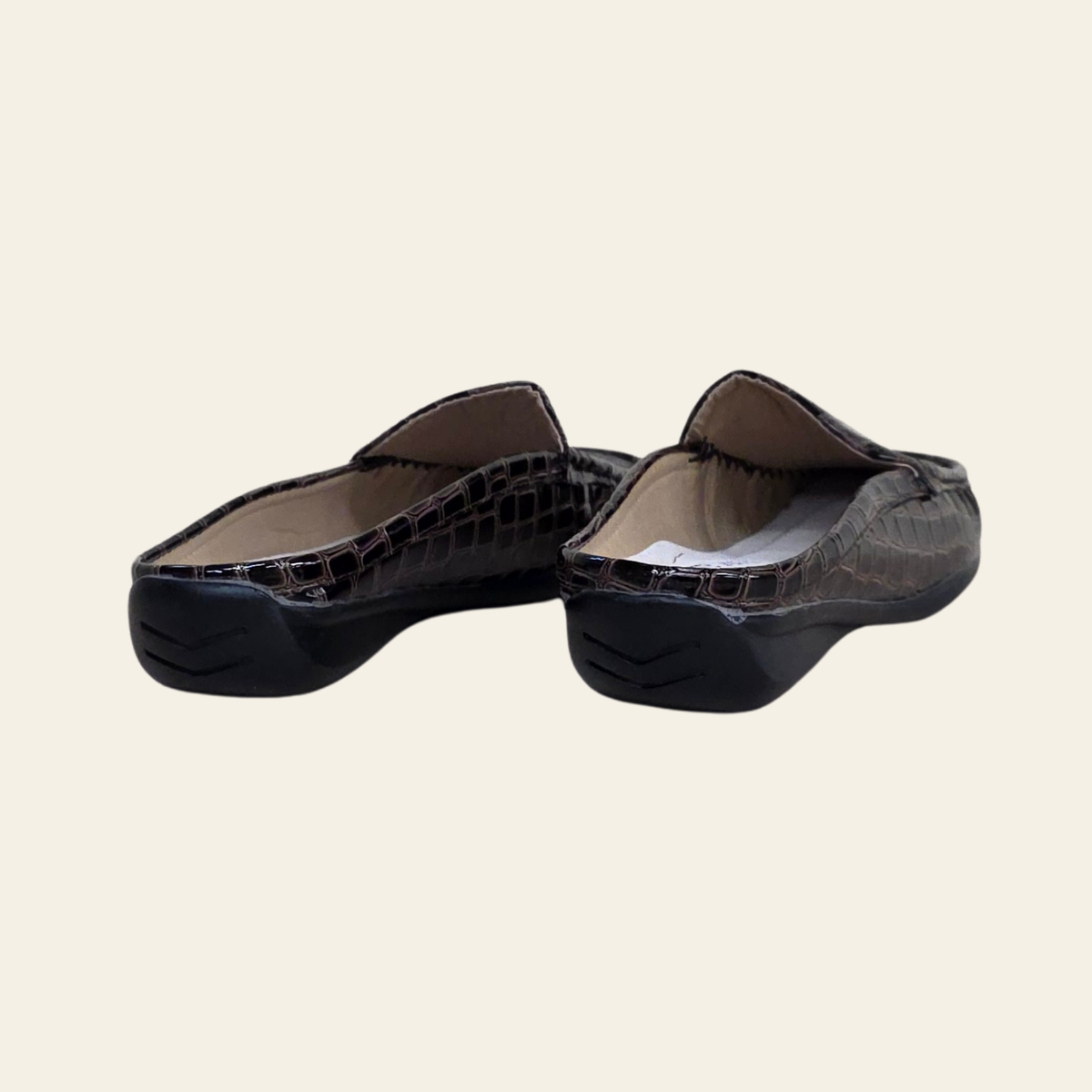 A pair of women's slip-on flats with a glossy crocodile-embossed texture in black and dark brown, shown from a three-quarters angle on a light cream background.