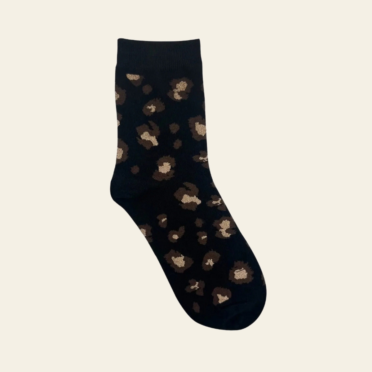 A single black crew sock with an all-over leopard print pattern in shades of brown and beige, displayed against a solid off-white background.