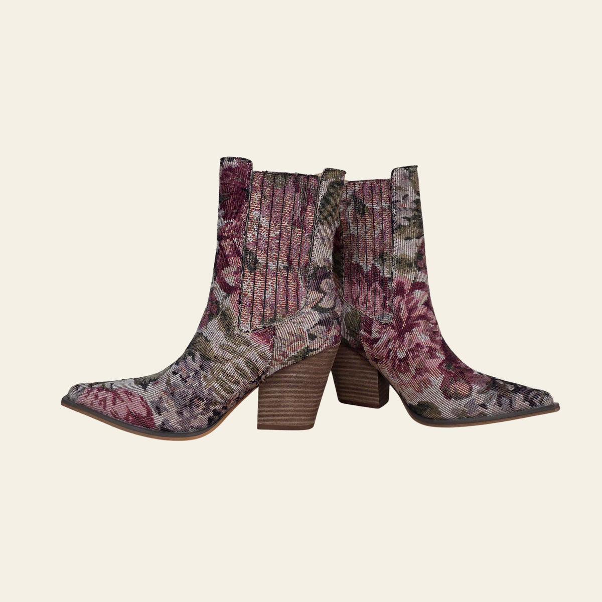 A pair of pointed-toe ankle boots with a floral tapestry pattern in dusty pink, purple, and green, featuring ribbed knit side panels and stacked wooden block heels, shown against a solid cream background.