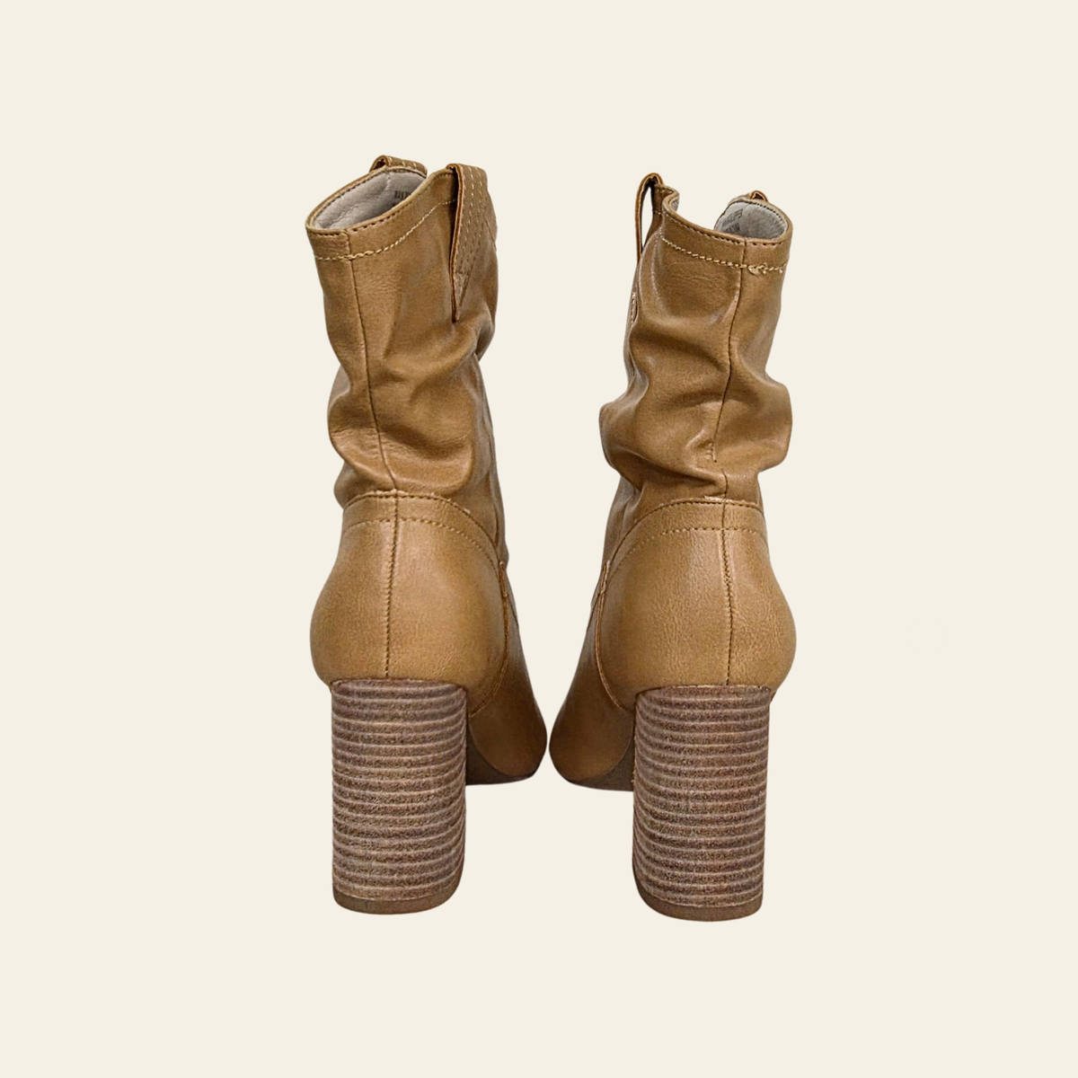 A pair of tan faux leather slouchy ankle boots with chunky stacked block heels, shown from the back on a light cream background.