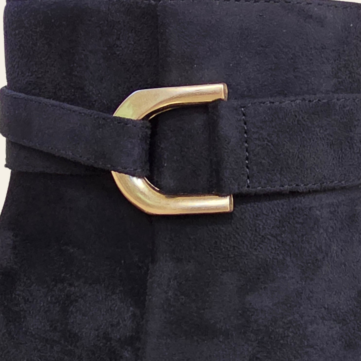 Close-up of a black faux suede belt with a polished gold-tone metal buckle on a dark garment.