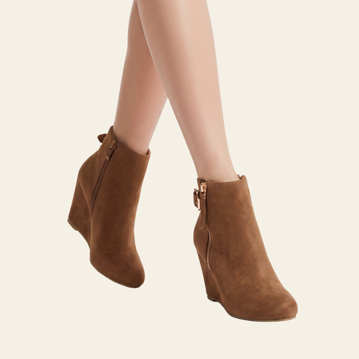 A pair of women's brown suede ankle boots with wedge heels and side zippers, shown on a model's feet against a light cream background.