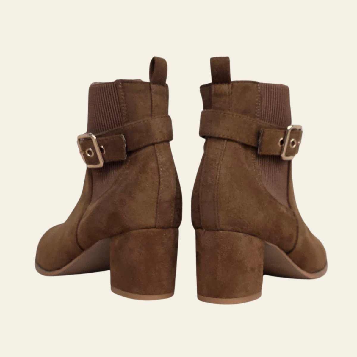 A pair of women's brown suede ankle boots with block heels and a matching ankle strap featuring a square buckle, shown from the back on a light cream background.