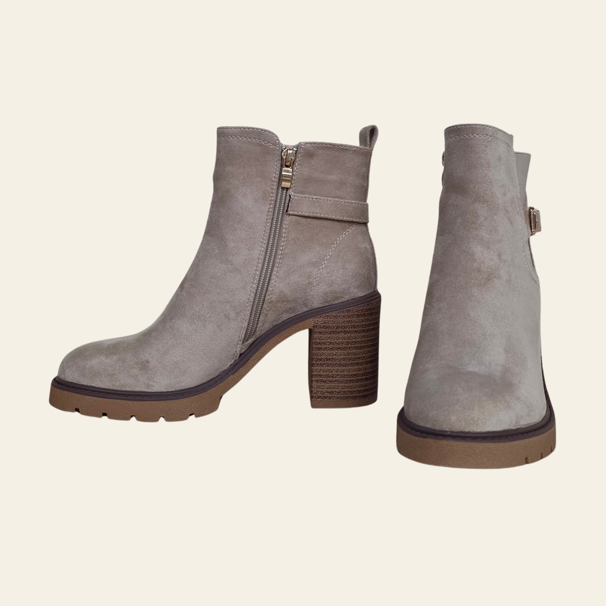 A pair of taupe gray suede ankle boots with brown block heels and soles, shown from the side and back angles on a light cream background.