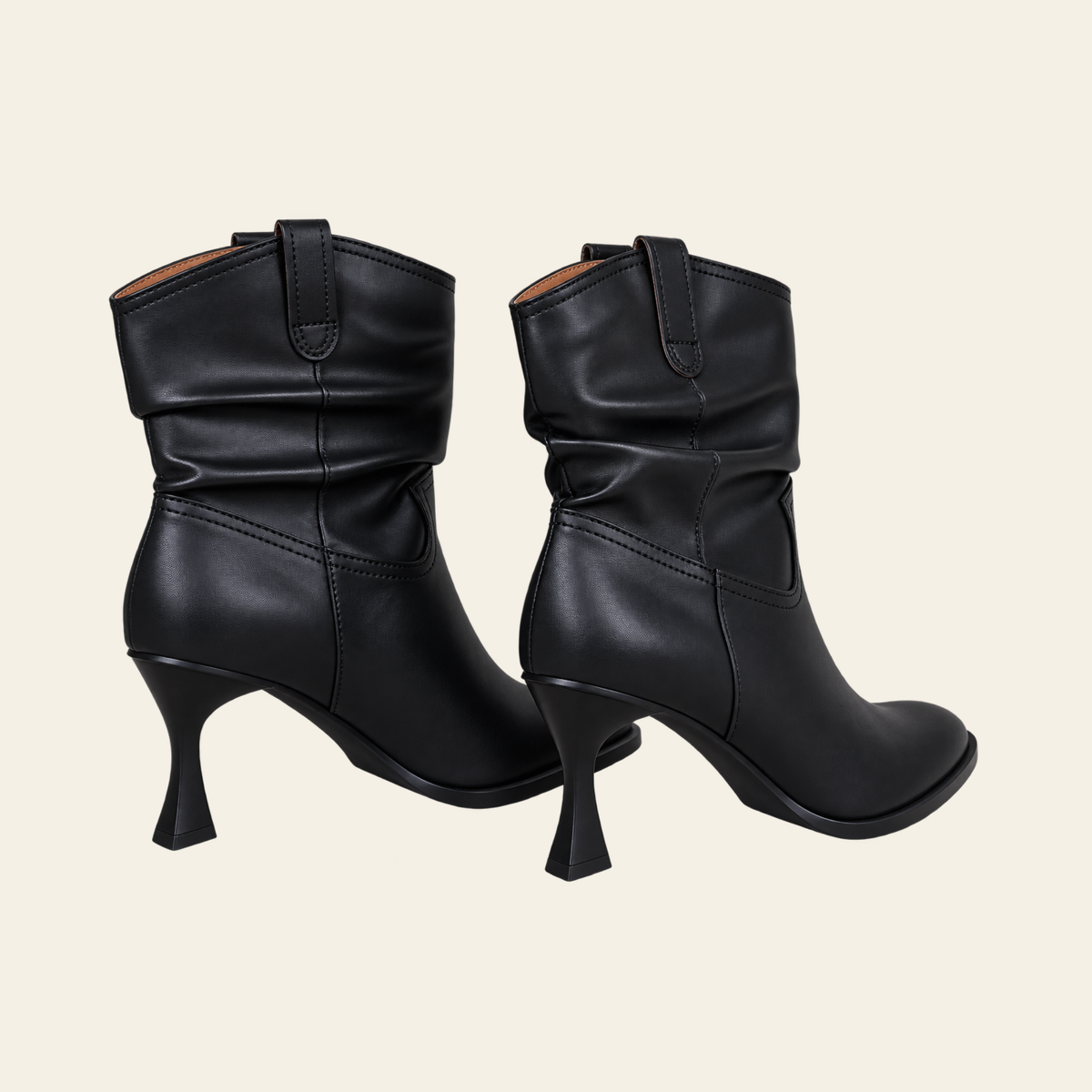 A pair of black leather ankle boots with a unique flared kitten heel and a draped, slouchy shaft, shown from the side against a light cream background.