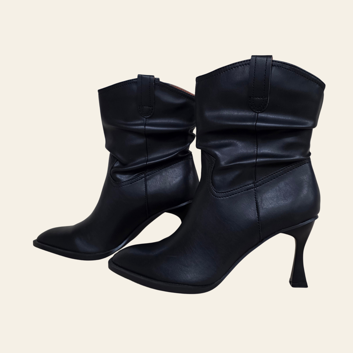 A pair of black leather slouchy ankle boots with kitten heels, shown against a solid light beige background.