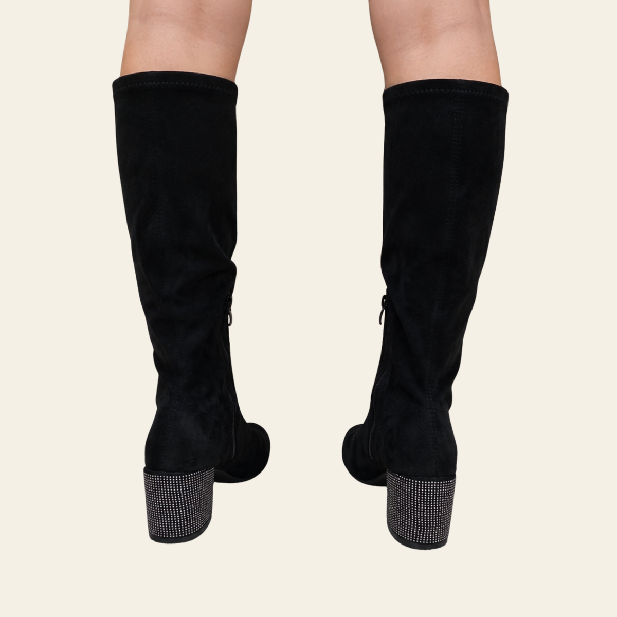 A pair of black ankle boots with high stiletto heels, platform soles, side zippers, and decorative rhinestone bows with gold fringe, shown against a solid light beige background.