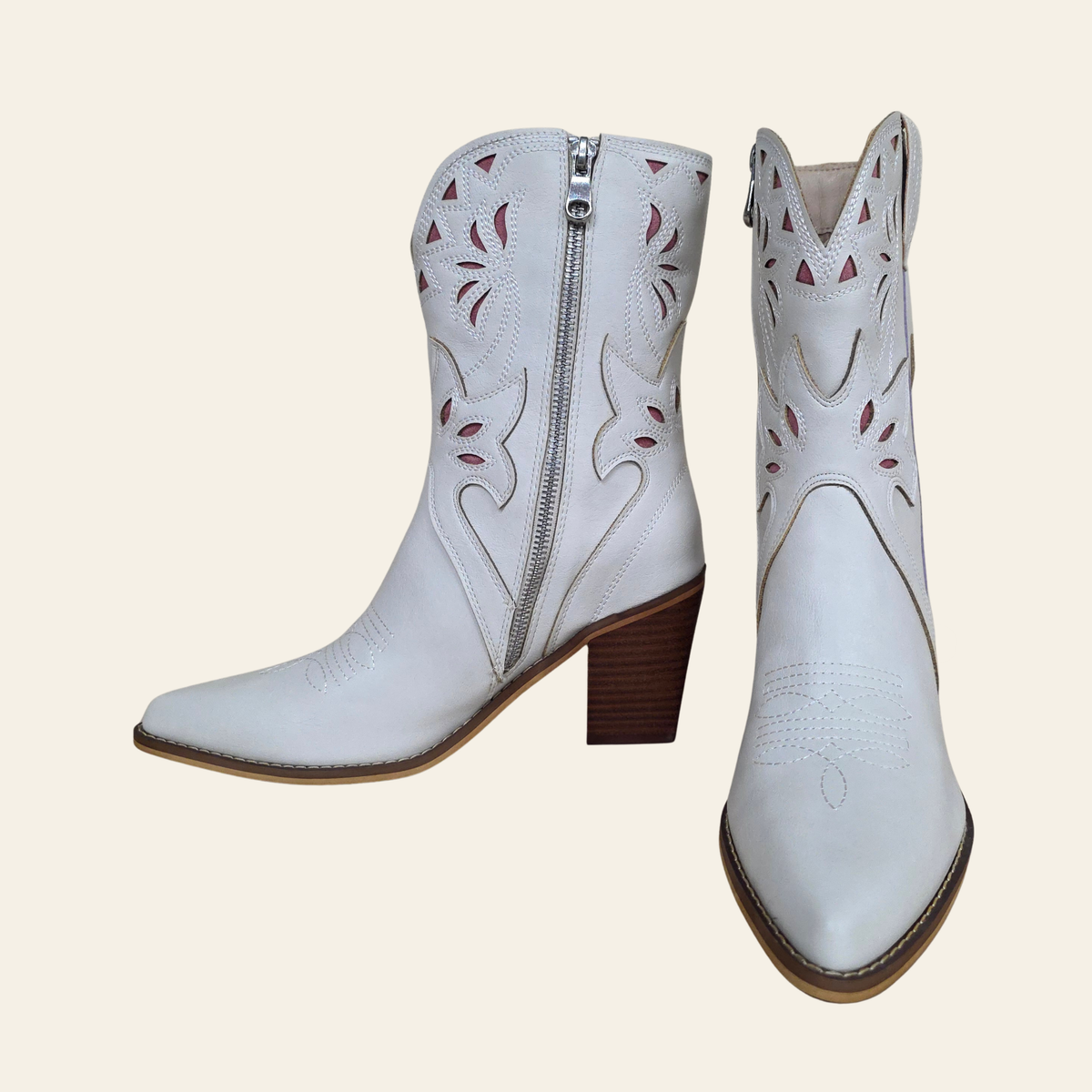 A pair of white western-style ankle boots with side zippers, featuring brown stacked block heels and brown outsole edges, shown from the side and front angles against a solid light beige background.
