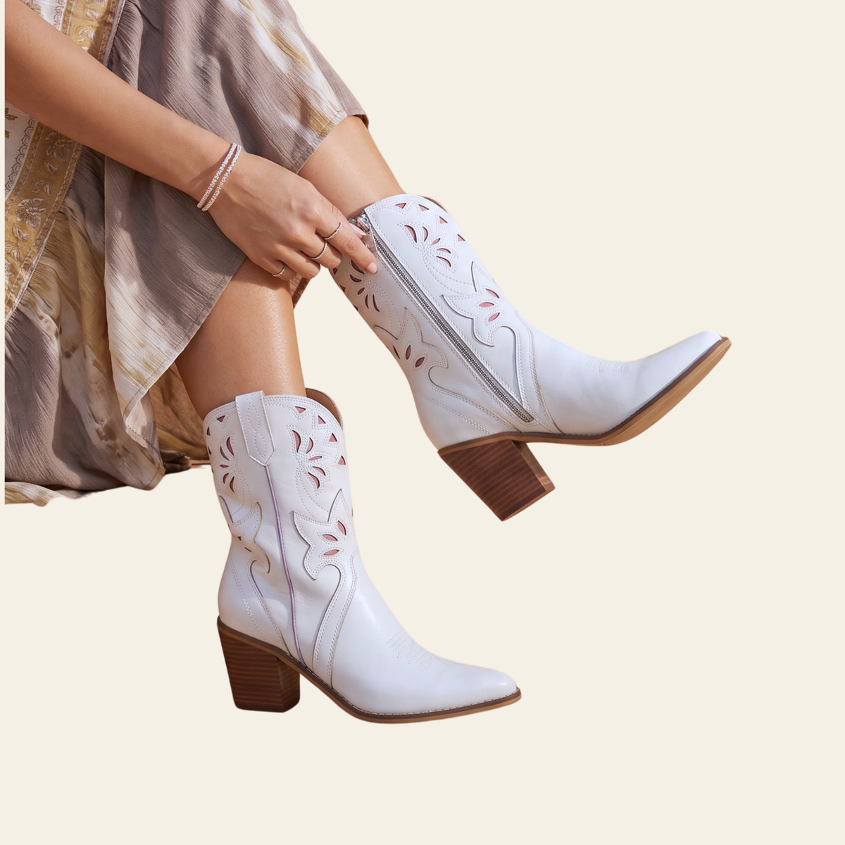 White western-style ankle boots with brown block heels and decorative cutout stitching, shown on a model seated against a light beige background.