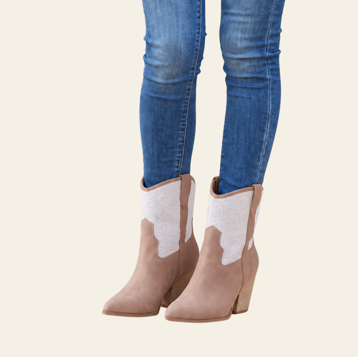 A person wearing blue skinny jeans and taupe western-style ankle boots with white embroidered shaft panels, shown against a plain light beige background.