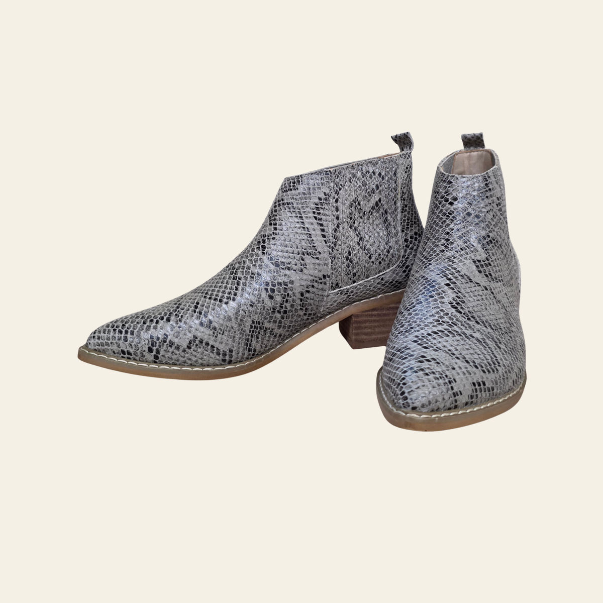 A pair of women's pointed-toe ankle boots featuring a gray and black snakeskin pattern, with a stacked brown block heel, shown against a solid light beige background.