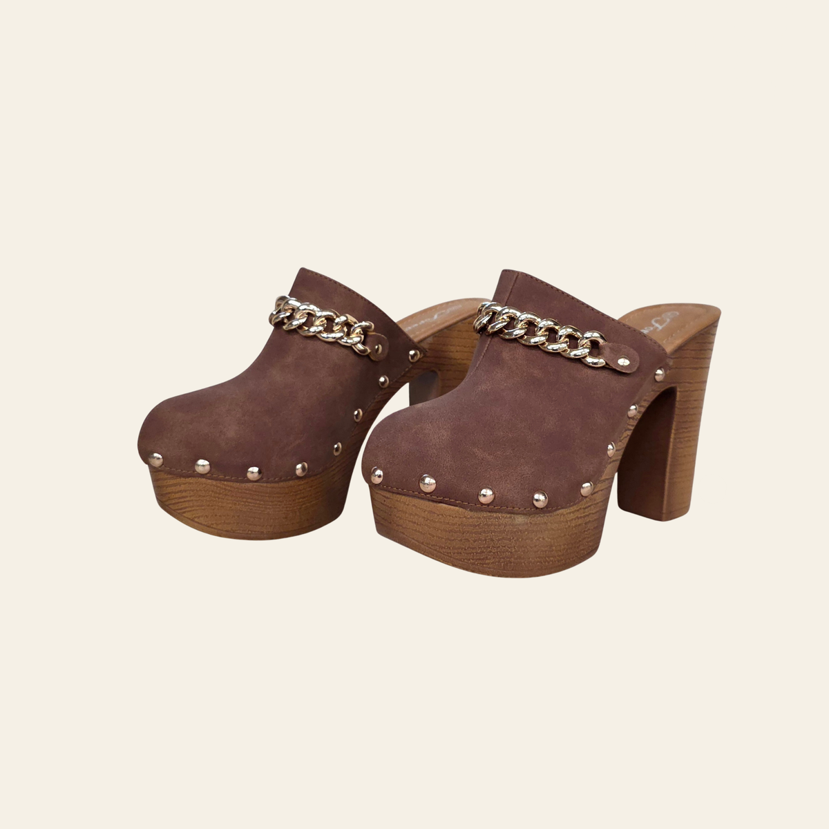 A pair of women's brown suede clogs with chunky wooden platform heels, silver-tone studs, and a gold-tone chain detail across the top, shown against a solid cream background.