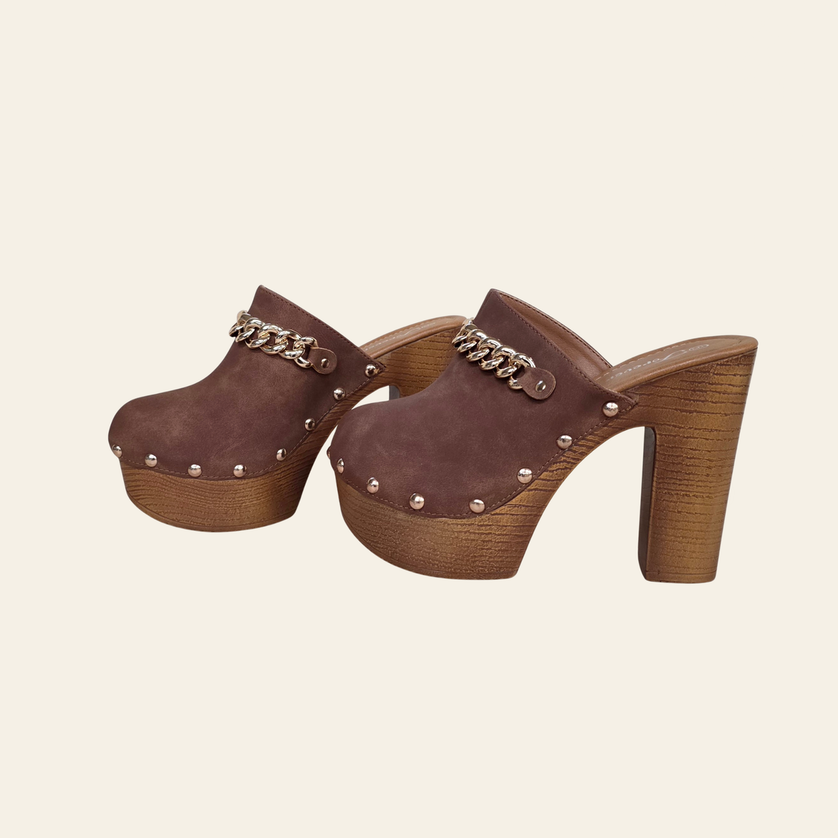 A pair of women's brown suede clog-style mule heels with chunky wooden platform soles and block heels, decorated with silver-tone studs and a chain detail across the top, shown on a light cream background.