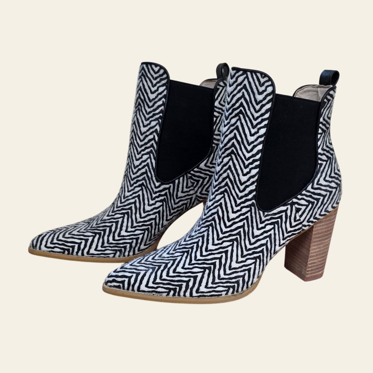 A pair of women's ankle boots featuring a black and white herringbone pattern on the toe and block heel, with black elastic side panels, shown against a solid light beige background.