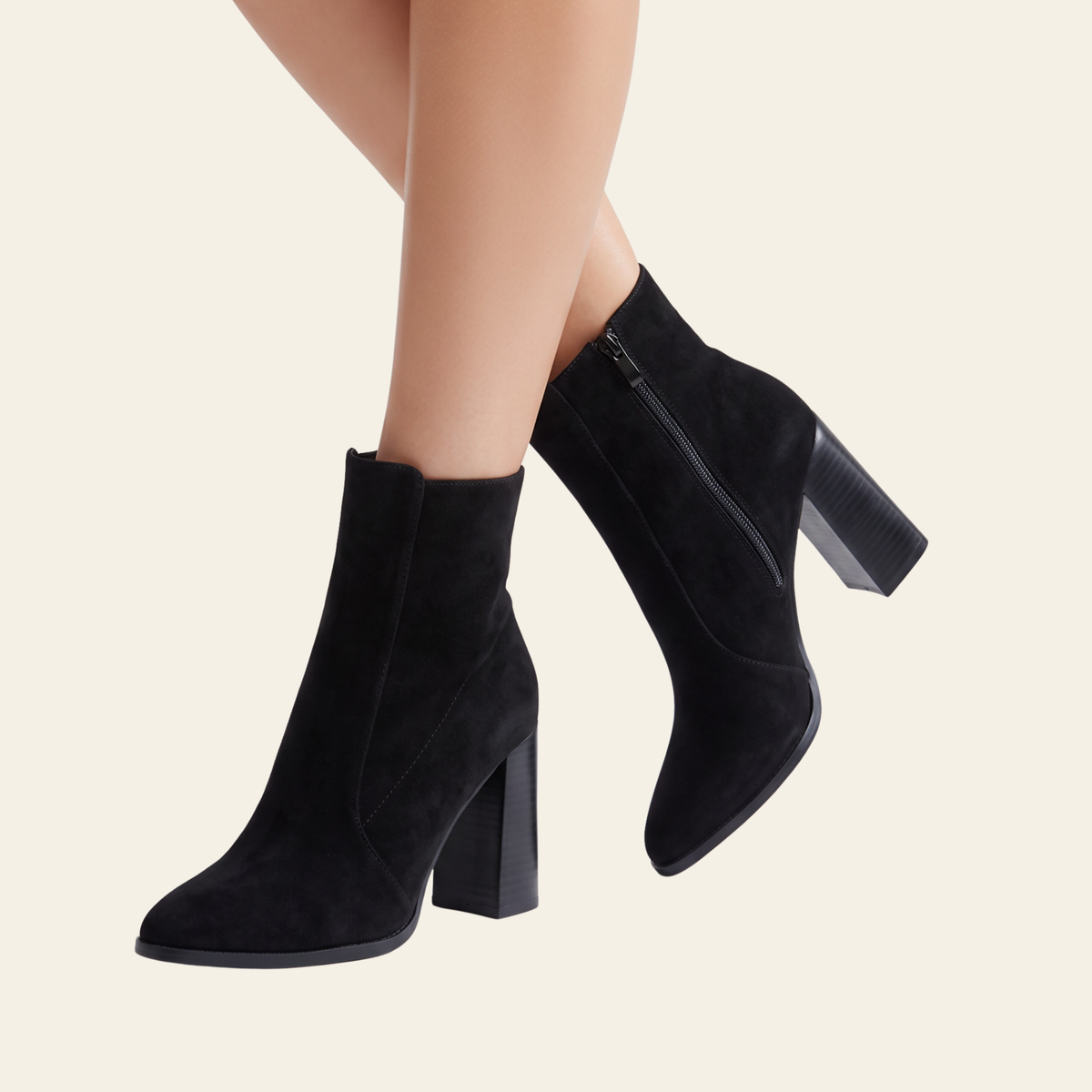 Black suede ankle boots with block heels and side zippers, shown on a model's feet against a light cream background.
