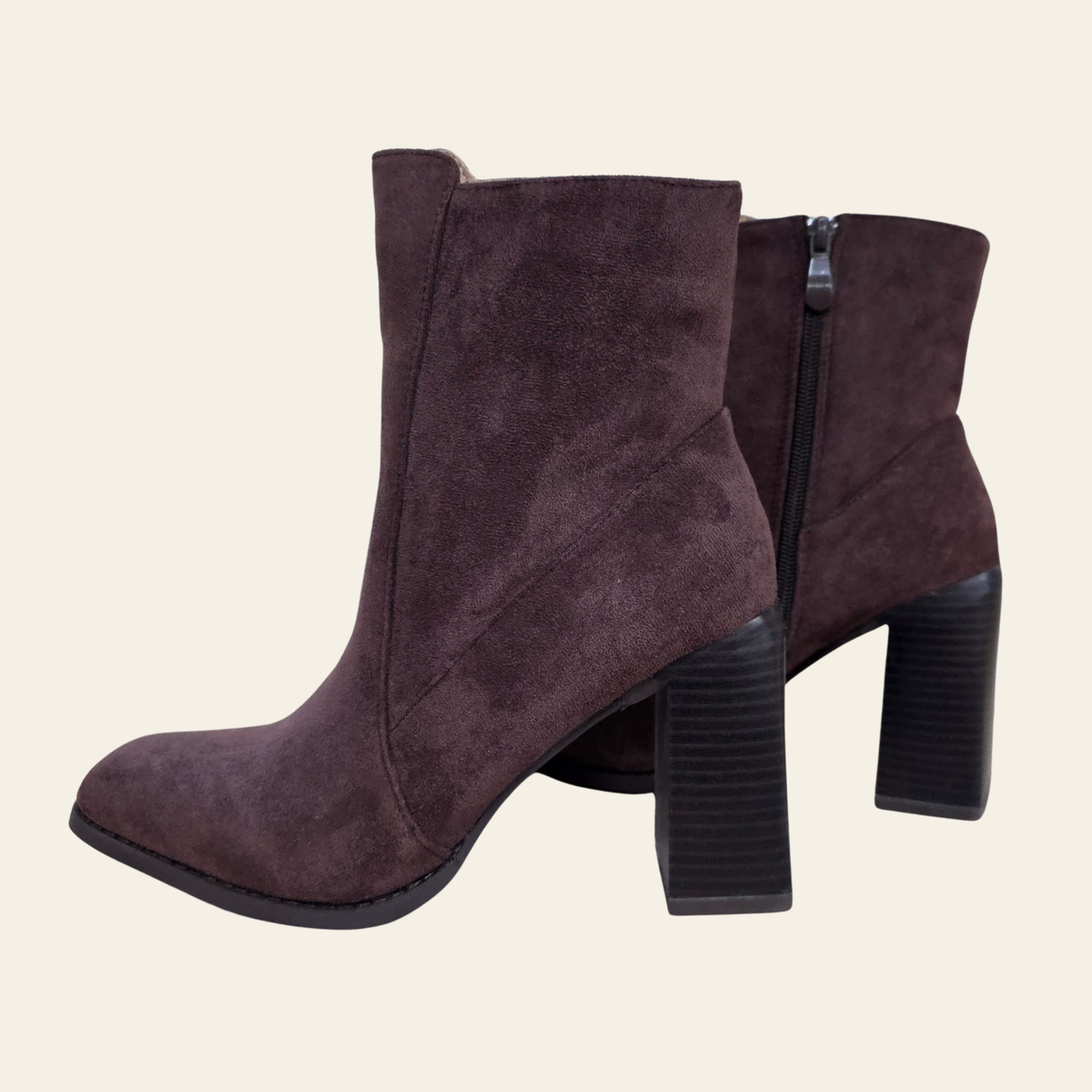 A pair of brown faux suede ankle boots with chunky black block heels, shown from a side profile view against a solid light beige background.