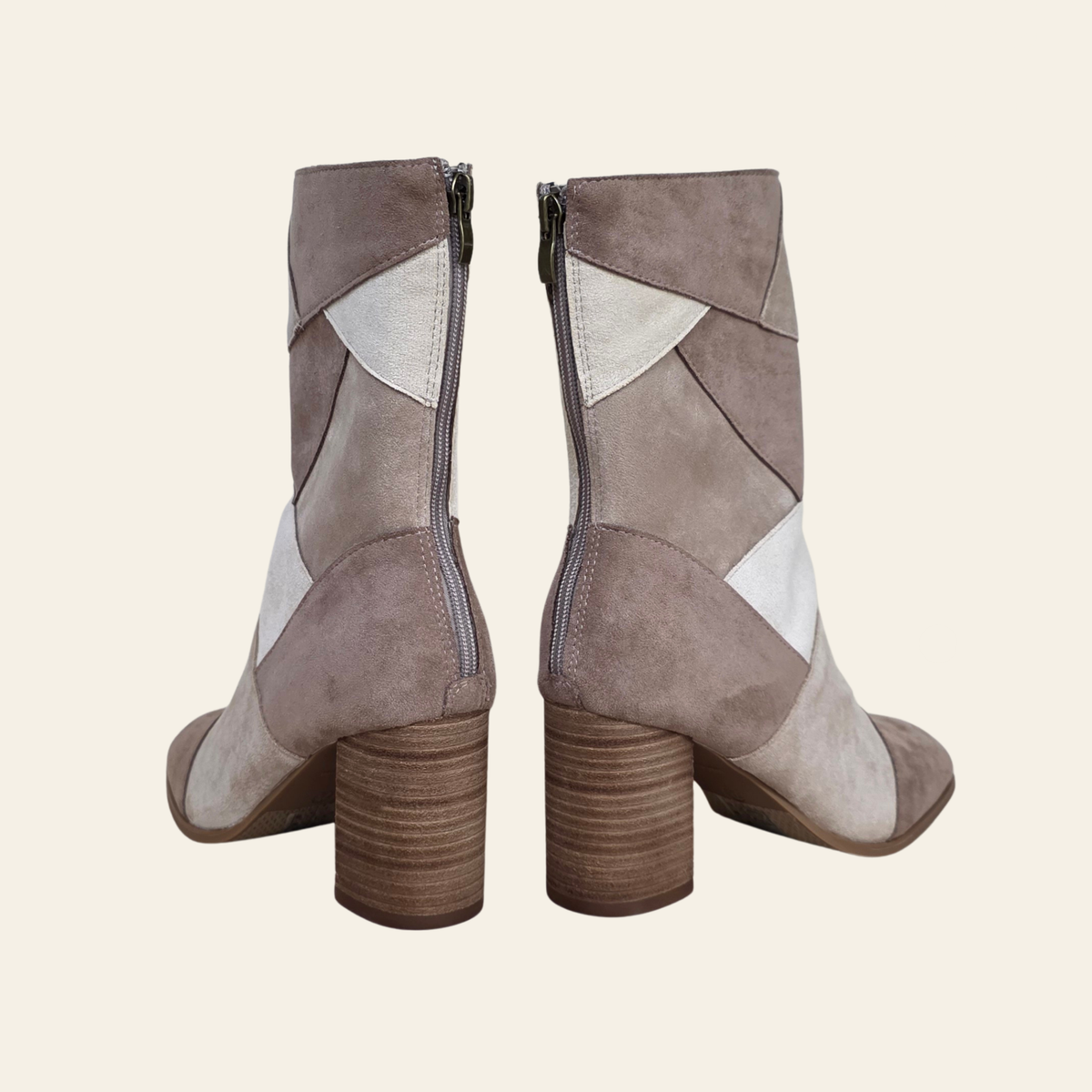 A pair of women's mid-calf ankle boots shown from the back, featuring a taupe suede upper with contrasting light beige and white geometric patches, a brown block heel, and a side zipper.