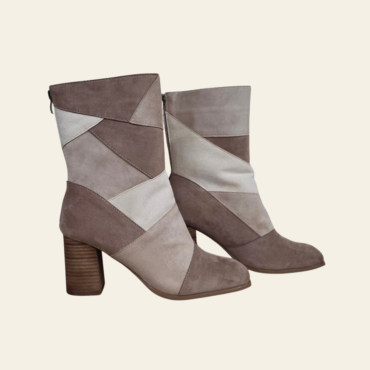 A pair of mid-calf ankle boots with a geometric patchwork design in taupe, beige, and light gray suede, featuring a chunky brown block heel, shown against a solid cream background.