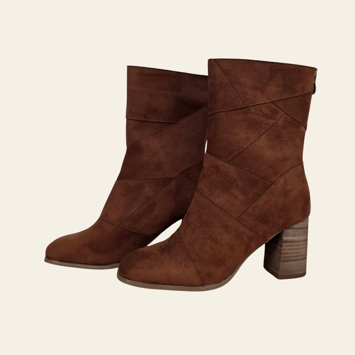 A pair of brown suede ankle boots with a geometric crisscross pattern on the shaft and a stacked block heel, shown against a solid off-white background.
