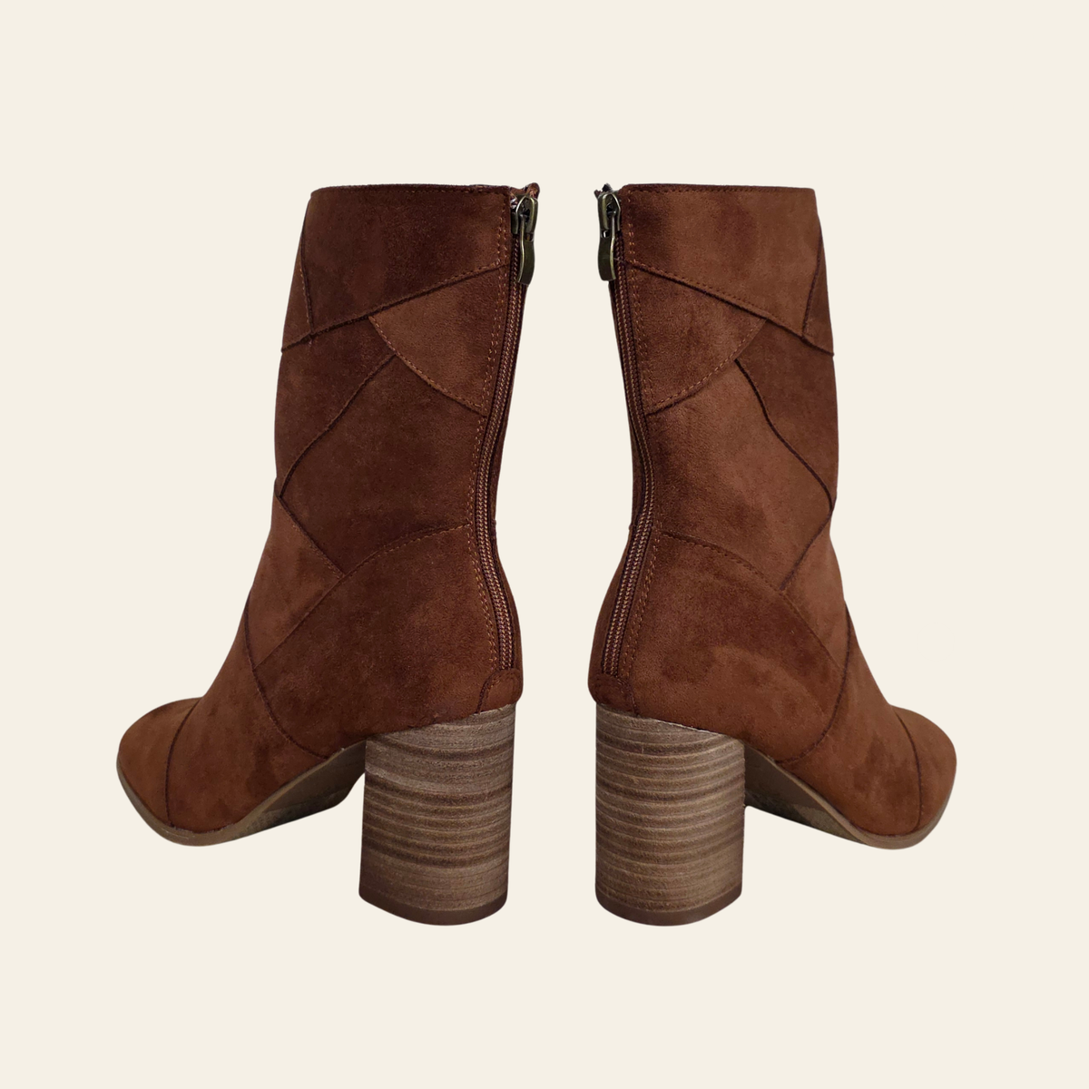 A pair of brown suede ankle boots with geometric paneling and stacked block heels, shown from the back on a light cream background.