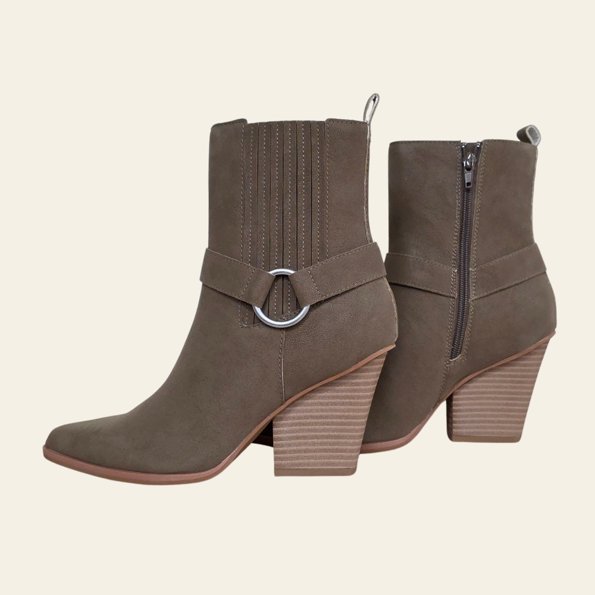 A pair of taupe-brown suede ankle boots with a side buckle strap and a zippered back, shown against a solid cream background.