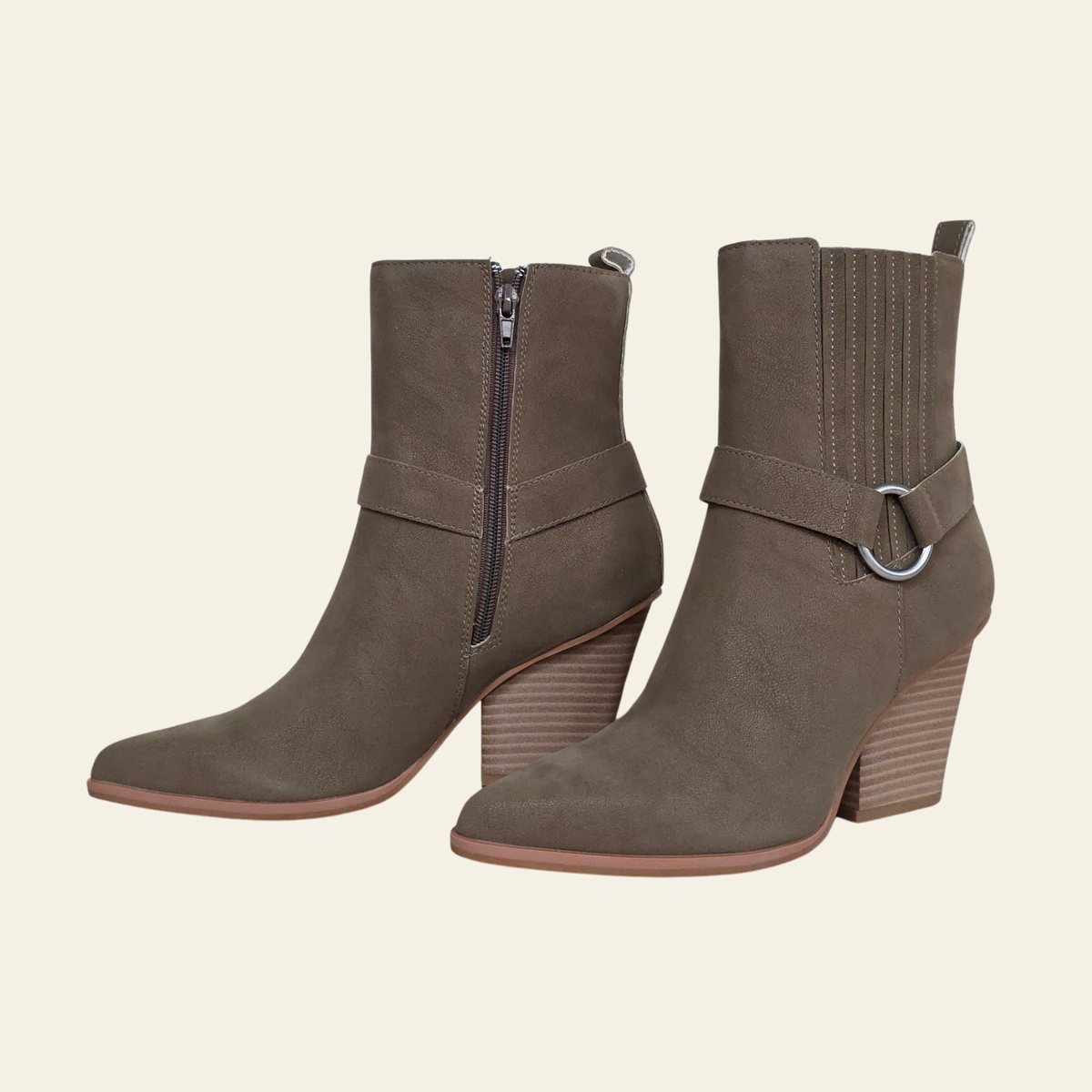 A pair of taupe-brown suede ankle boots with side zippers, wrap-around straps, and chunky stacked block heels, shown against a solid light beige background.