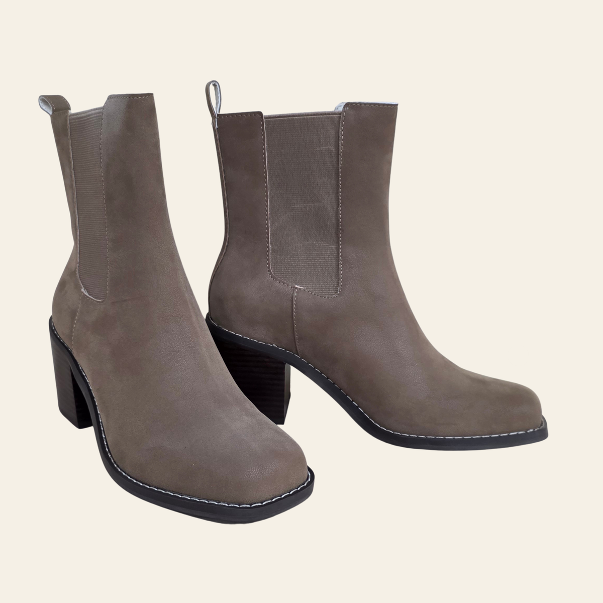 A pair of taupe-brown faux suede Chelsea-style ankle boots with block heels, displayed against a solid light beige background.