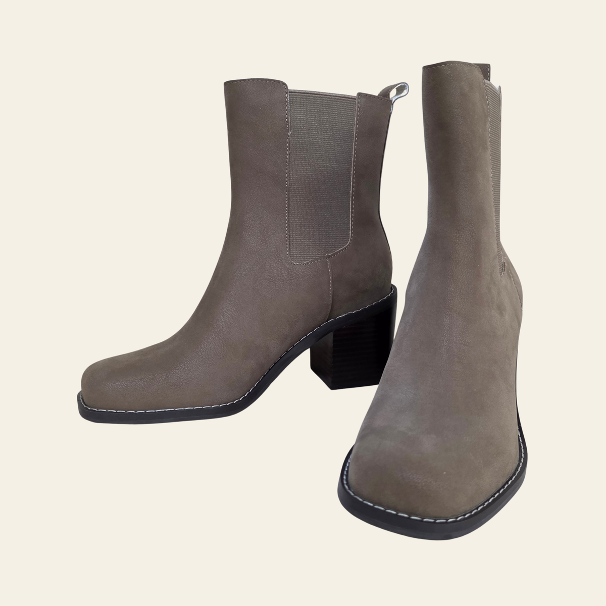 A pair of taupe-brown faux suede ankle boots with black block heels and elastic side panels, shown against a solid light beige background.