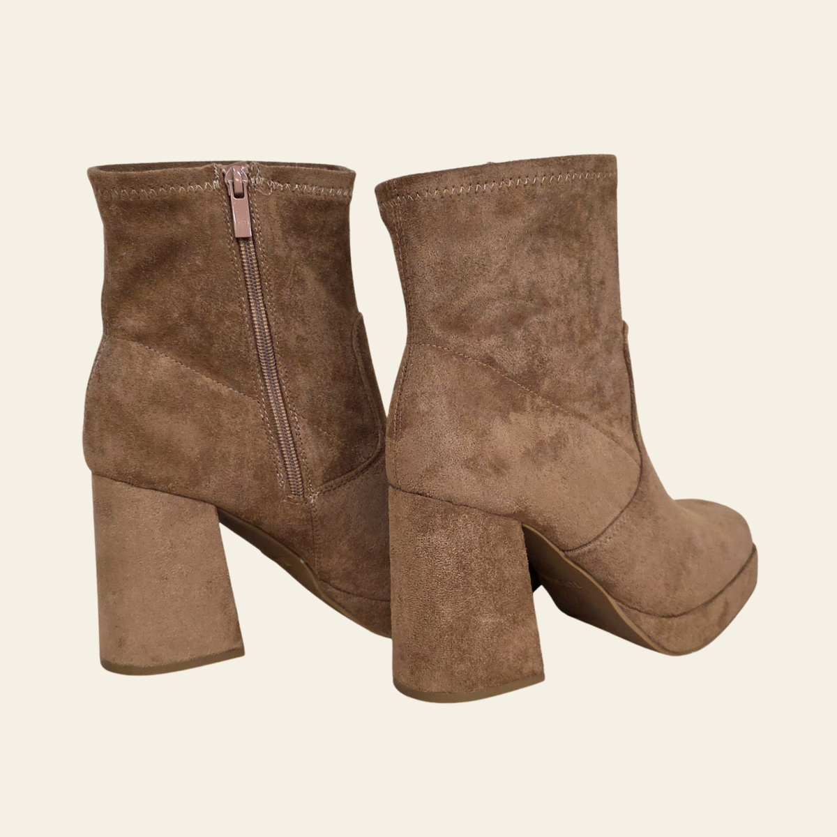 A pair of women's ankle boots in brown suede, featuring a chunky block heel, platform sole, and a side zipper on the back of one boot, shown against a solid off-white background.