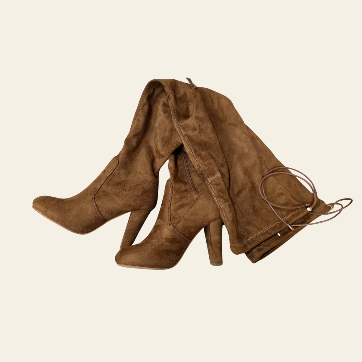 A pair of brown suede over-the-knee boots with high block heels and side laces, displayed on a solid light beige background.