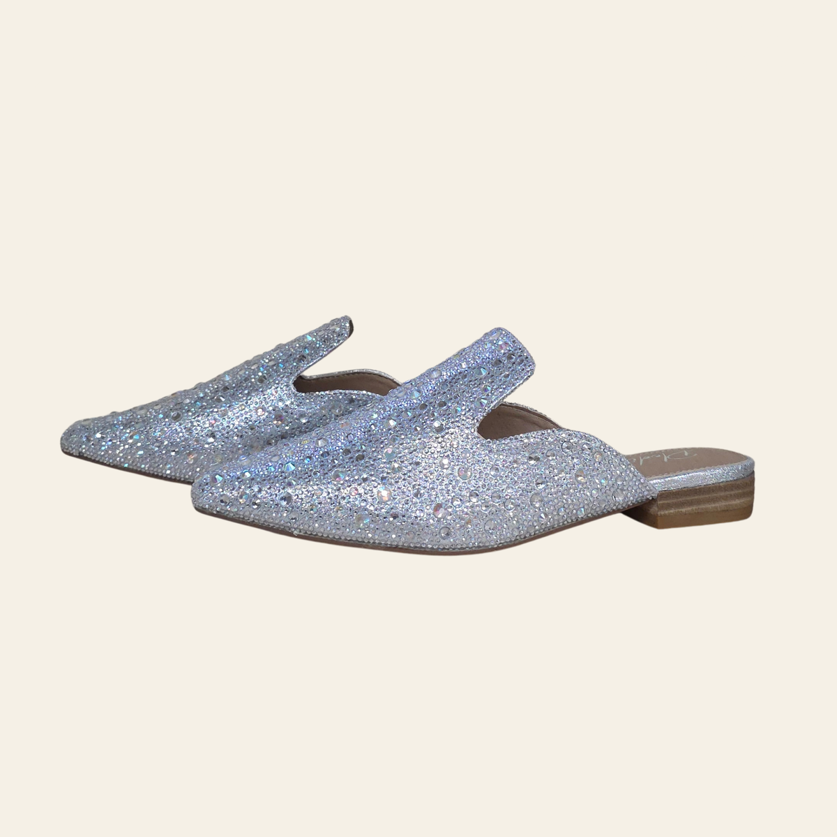 A pair GEM  pointed-toe mule flats covered in shimmering rhinestones, shown against a solid light beige background.