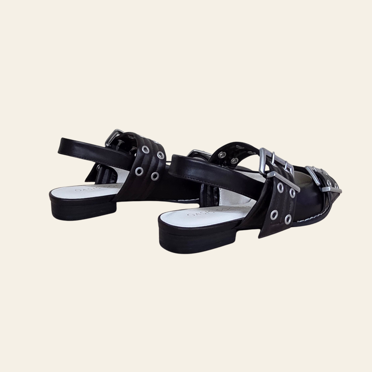 A pair of brown vegan leather ballet flats with multiple straps, silver-tone grommets, and buckles, shown against a solid light beige background.