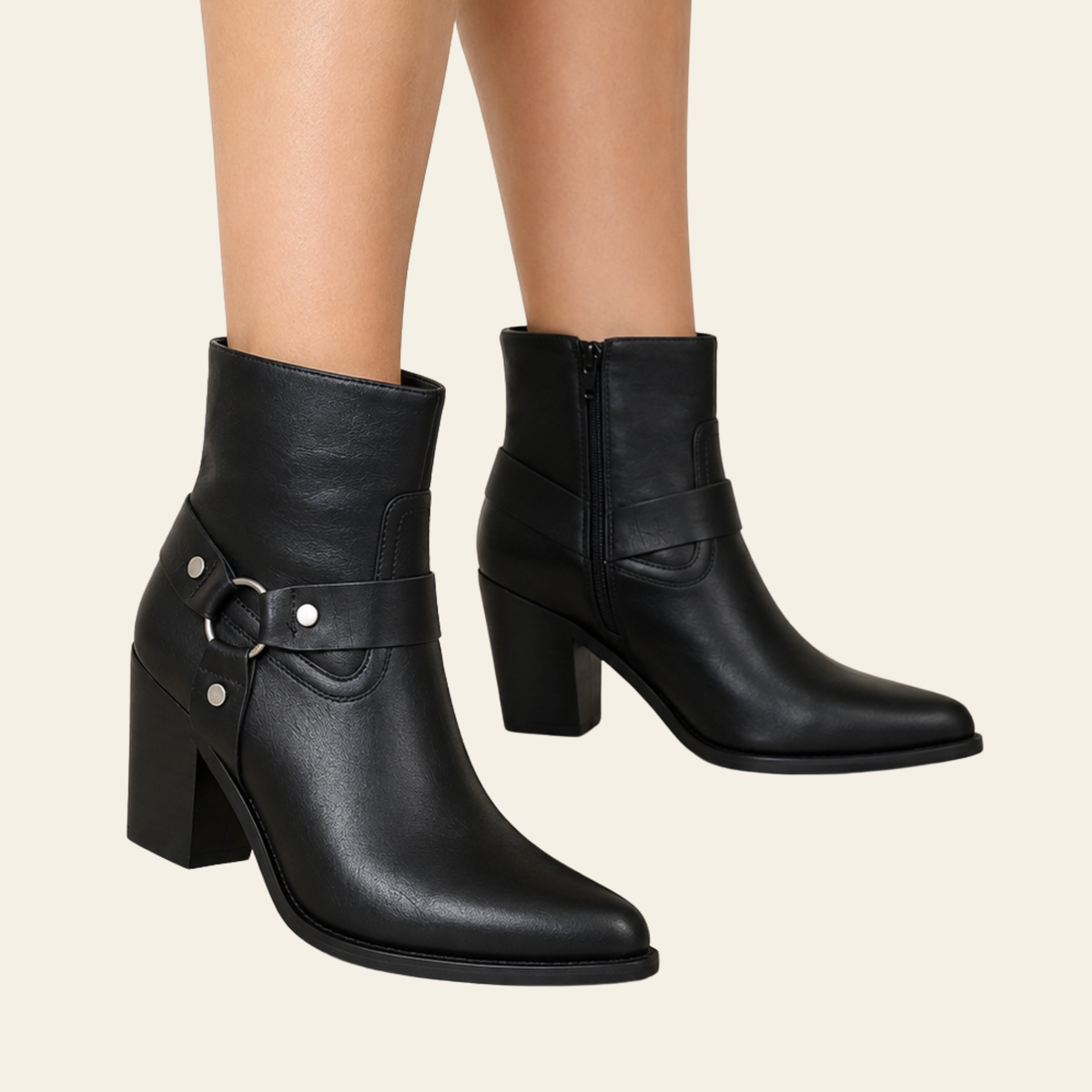 Black leather ankle boots with block heels and side buckle straps, shown on a model's feet against a light beige background.