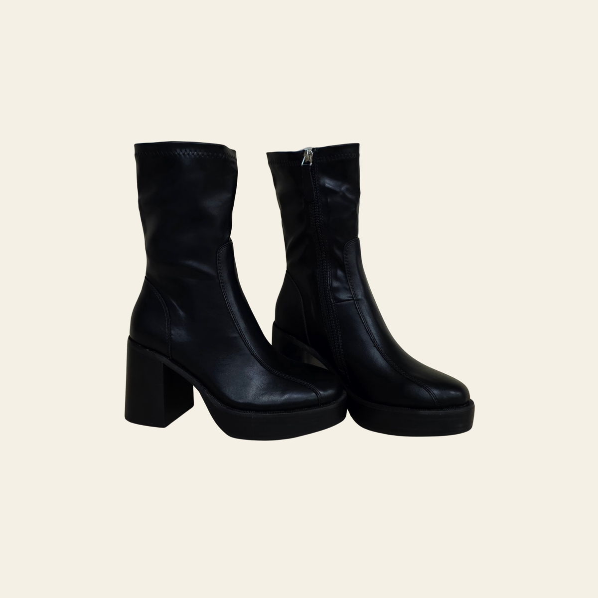 A pair of black leather ankle boots with chunky block heels and platform soles, shown against a solid light beige background.