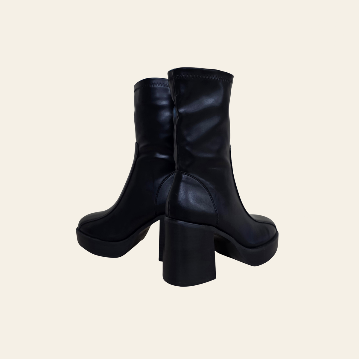 A pair of black leather ankle boots with chunky block heels and platform soles, shown from a three-quarters angle against a solid light beige background.