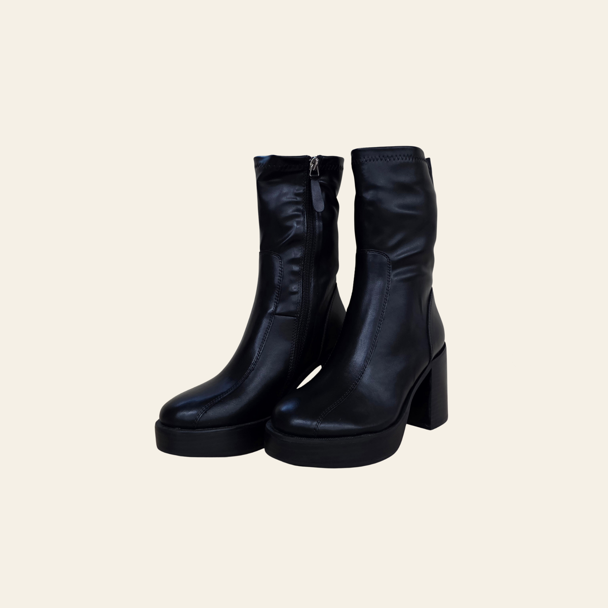 A pair of black leather ankle boots with a chunky block heel and platform sole, shown against a solid light beige background.