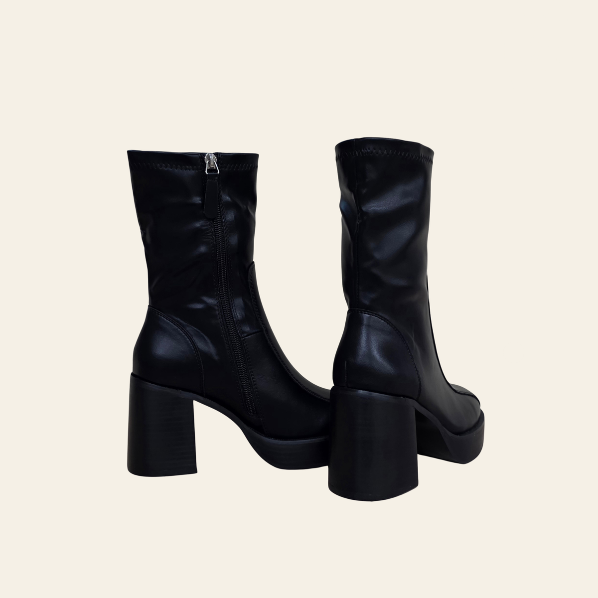 A pair of black leather ankle boots with chunky block heels and side zippers, shown from the back and side against a solid cream background.