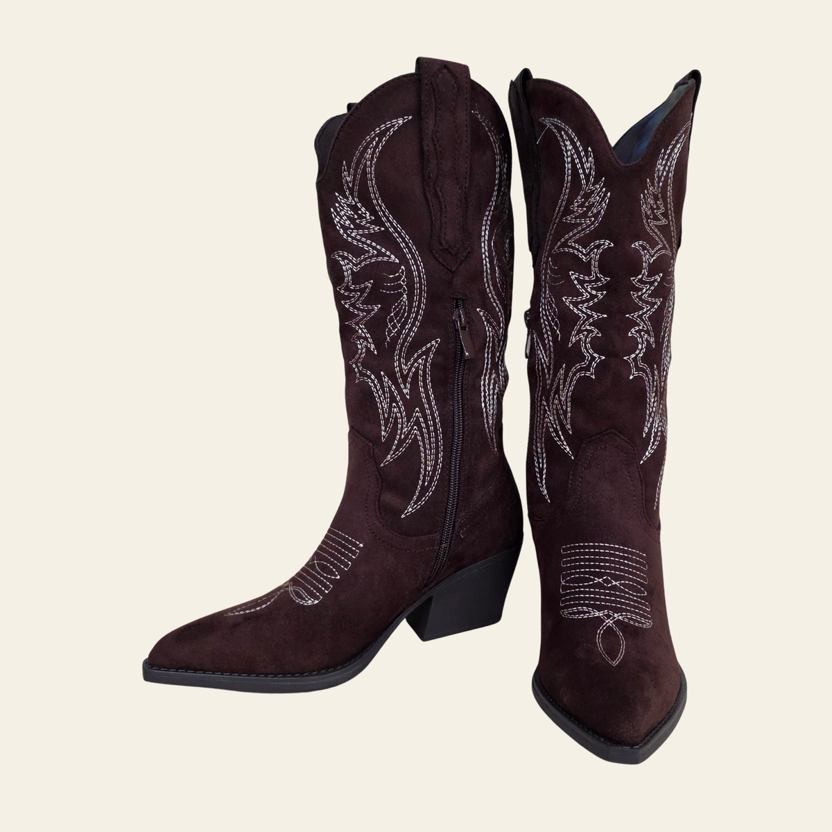 A pair of dark brown suede cowboy boots with silver rhinestone western embroidery, shown against a solid light beige background.