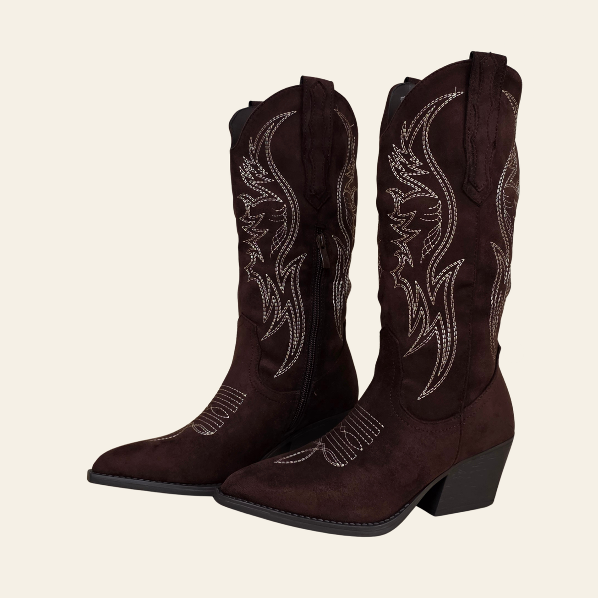 A pair of dark brown suede cowboy boots with white embroidered western patterns and silver rhinestone detailing, shown against a solid off-white background.