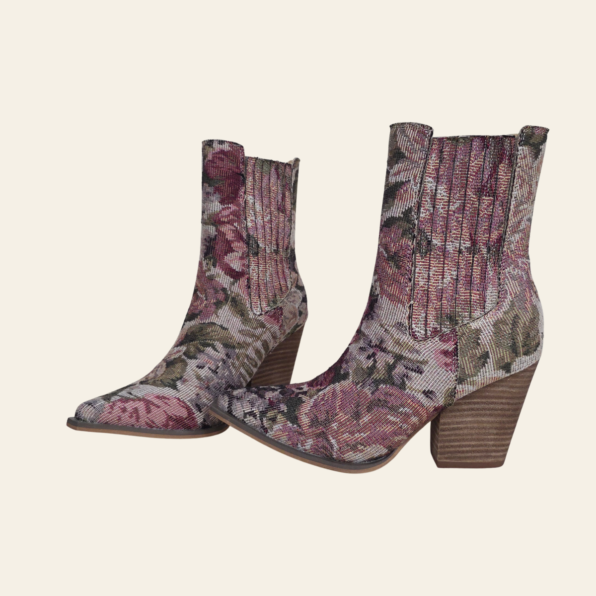 A pair of pointed-toe ankle boots with a floral tapestry pattern in dusty pink, mauve, and olive green, featuring a ribbed knit elastic side panel and a stacked wood-look block heel, shown against a solid cream background.