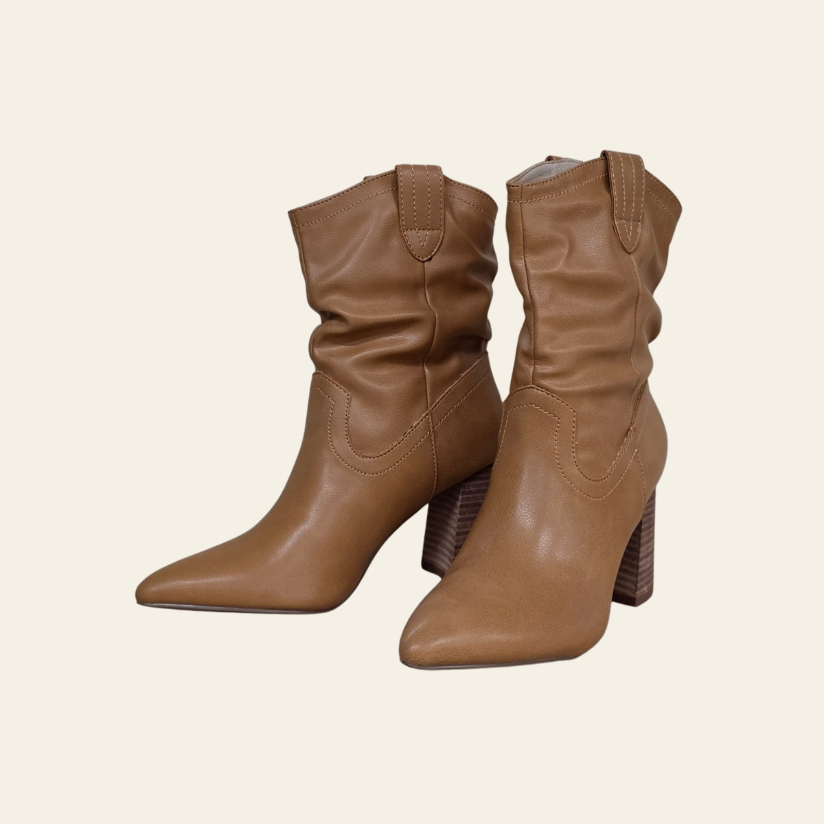 A pair of tan faux leather slouchy ankle boots with pointed toes and stacked block heels, shown against a solid light beige background.