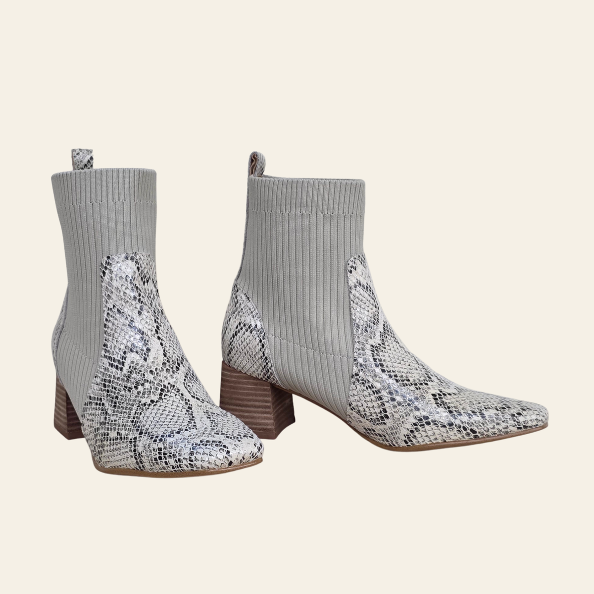 A pair of women's ankle boots featuring a gray ribbed knit sock-style upper and a snakeskin-patterned lower section and block heel, shown against a solid light beige background.
